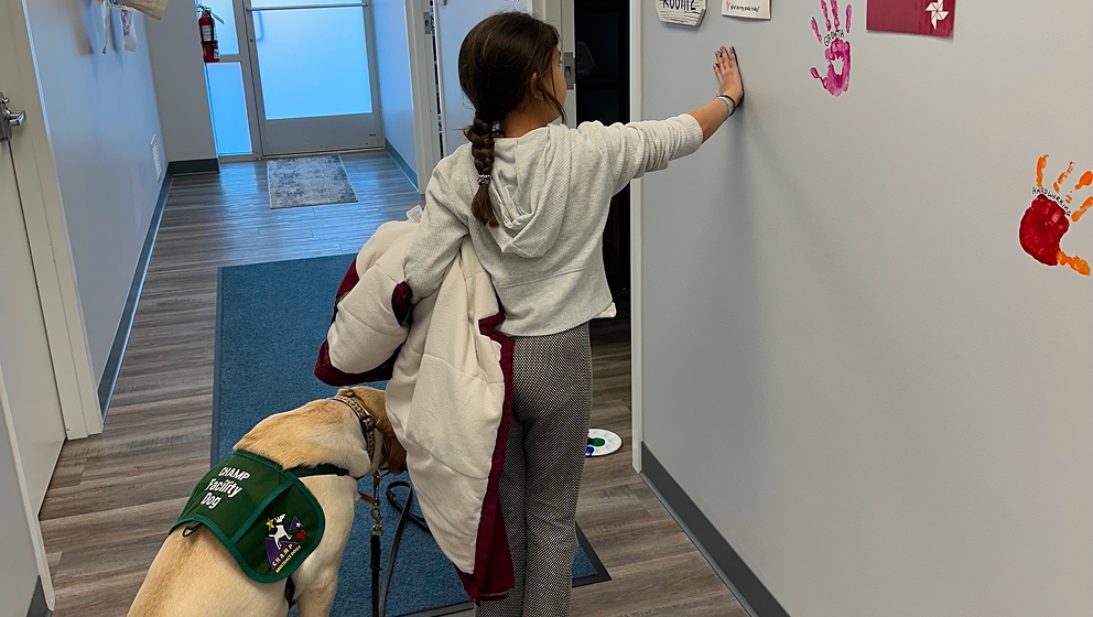 CHAMP Facility Dog supporting a child during a handprint celebration, likely marking a treatment milestone.